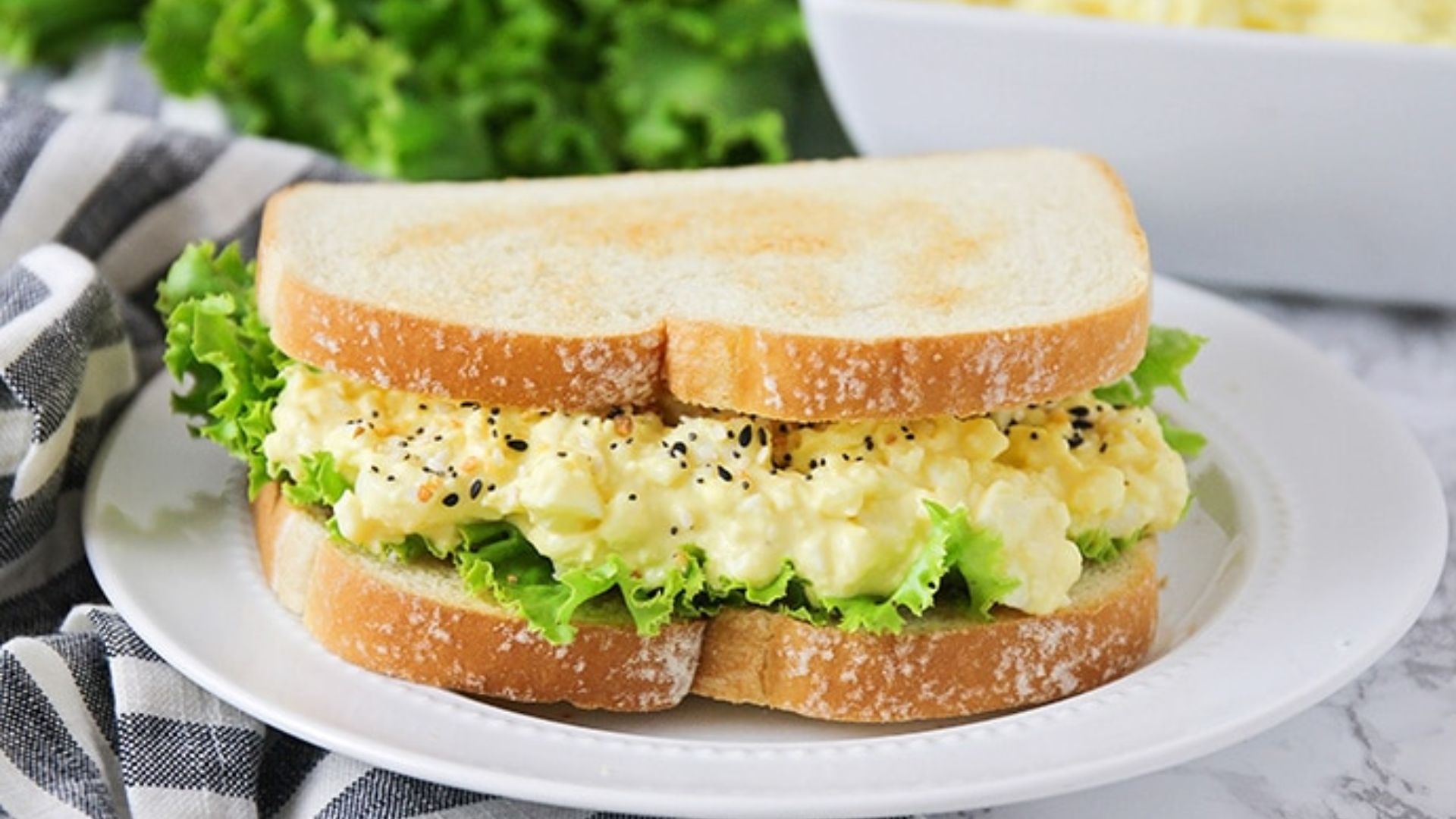 Creamy egg salad sandwich on whole-grain bread with chopped egg, celery, herbs and lettuce.