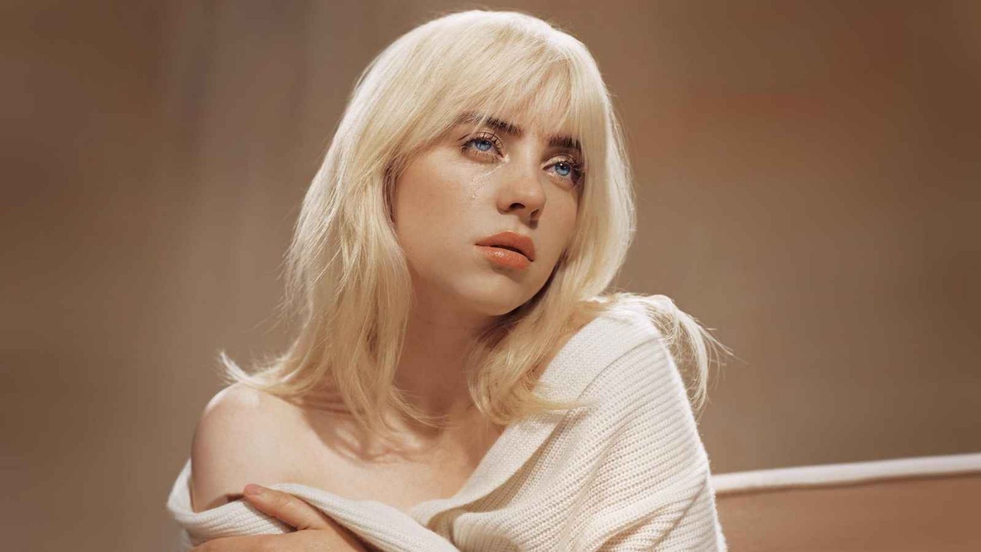 Album cover for Billie Eilish’s “Happier Than Ever,” showing the blonde artist looking up with a tear on her cheek while wearing an off-the-shoulder cream sweater.