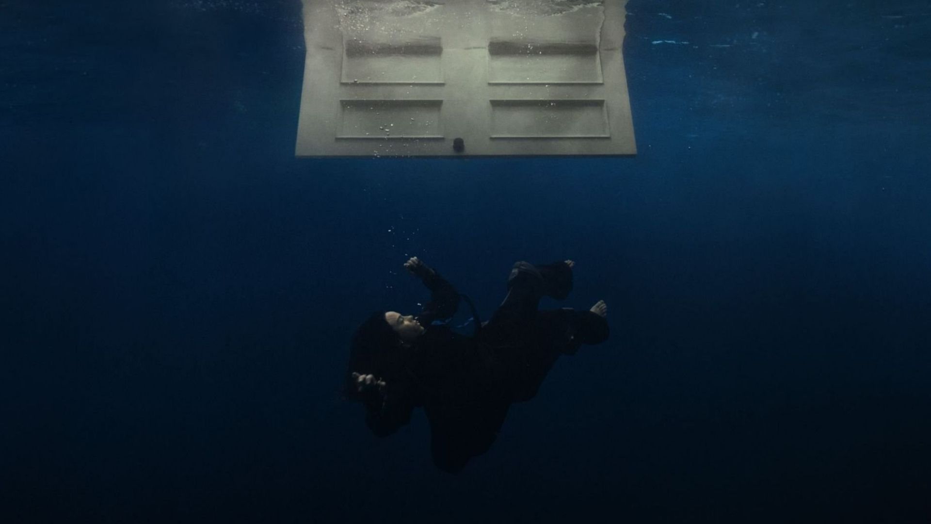 Album cover for Billie Eilish’s “HIT ME HARD AND SOFT,” depicting the artist floating or sinking underwater in a deep blue ocean beneath an open white door.