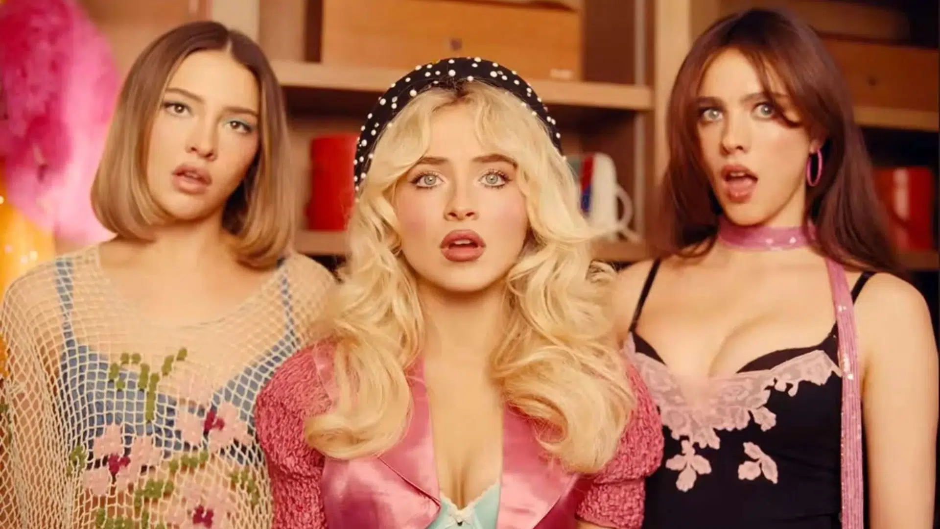 three women pose indoors in colorful retro outfits, with Sabrina carpenter centered between two brunettes