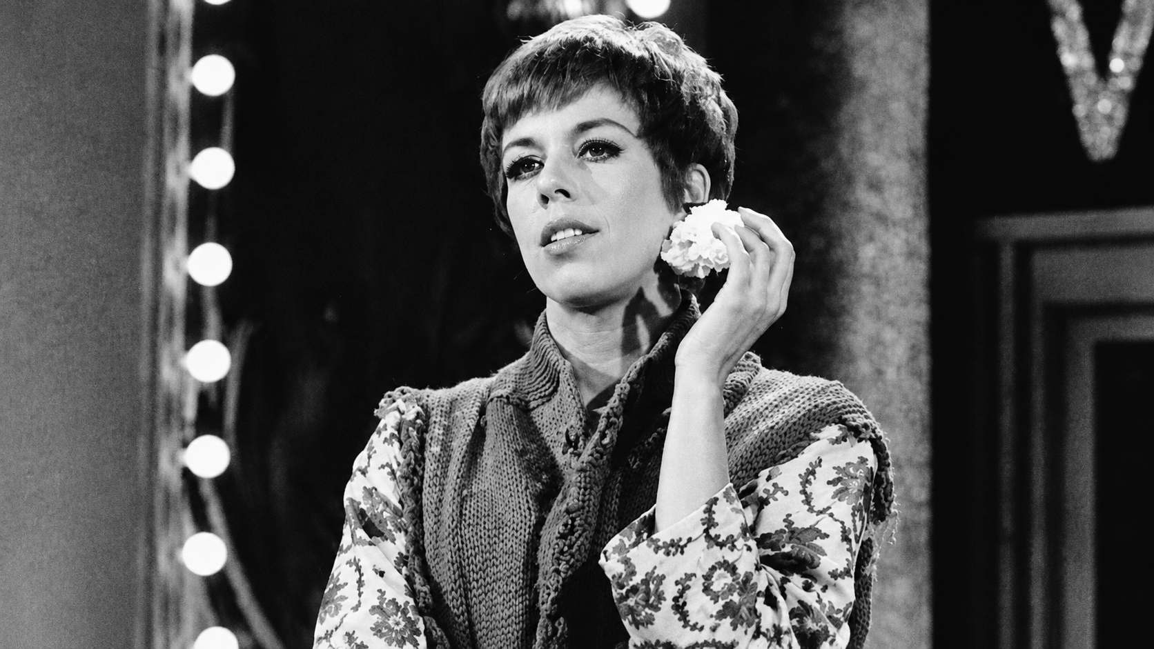 black and white vintage portrait of carol burnett holding a flower near her face on a theatrical stage with lights