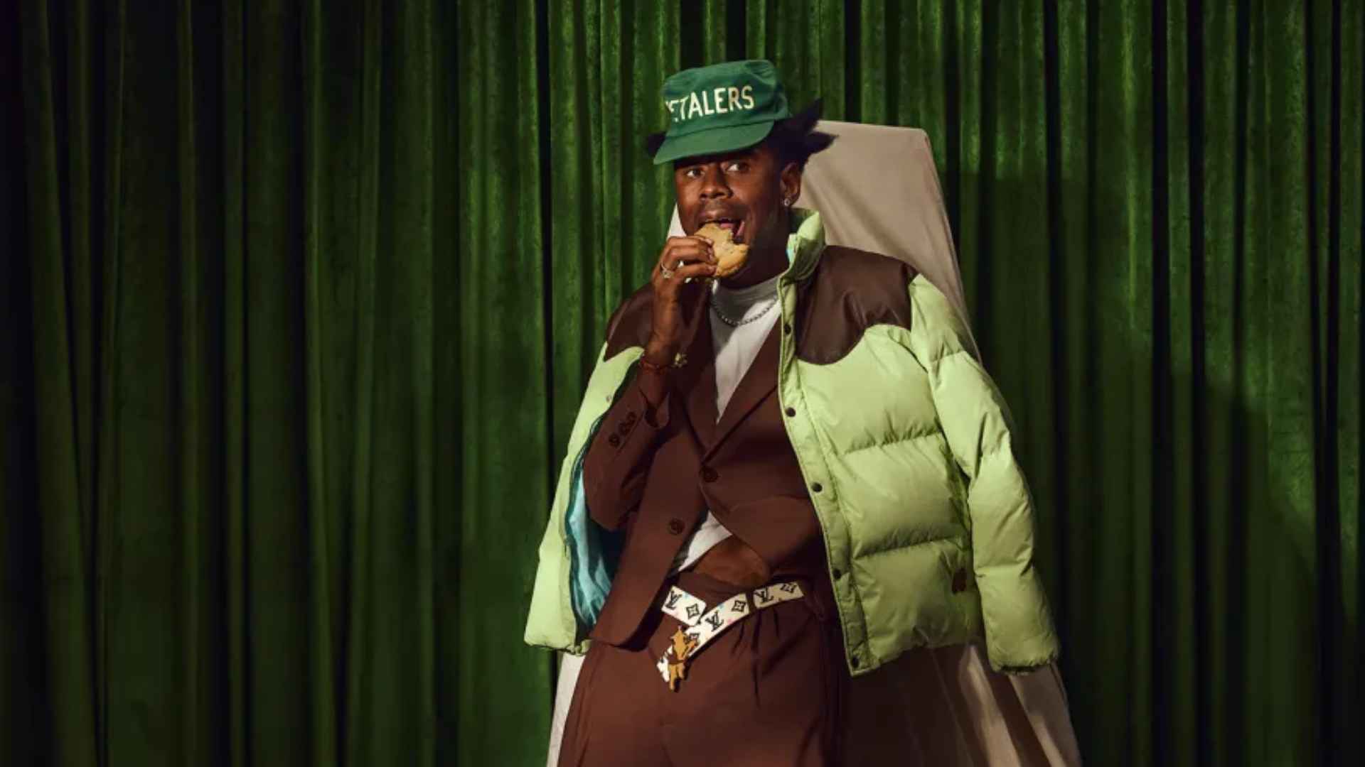 Tyler, The Creator performing on stage in a green and brown outfit with a matching hat and jacket.