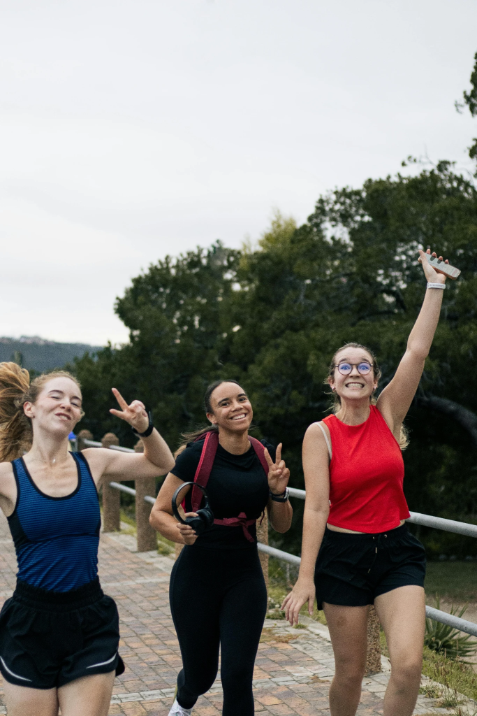 Three women jogging and smiling on a park pathway surrounded by greenery