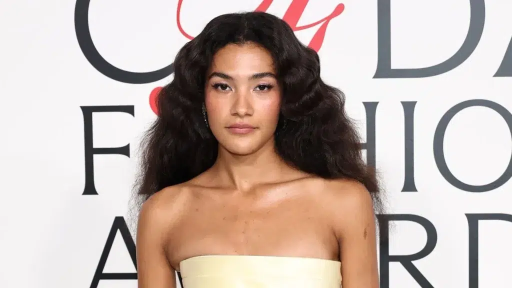 olivia dean wearing a strapless outfit at a red carpet event with voluminous hair and a neutral backdrop.