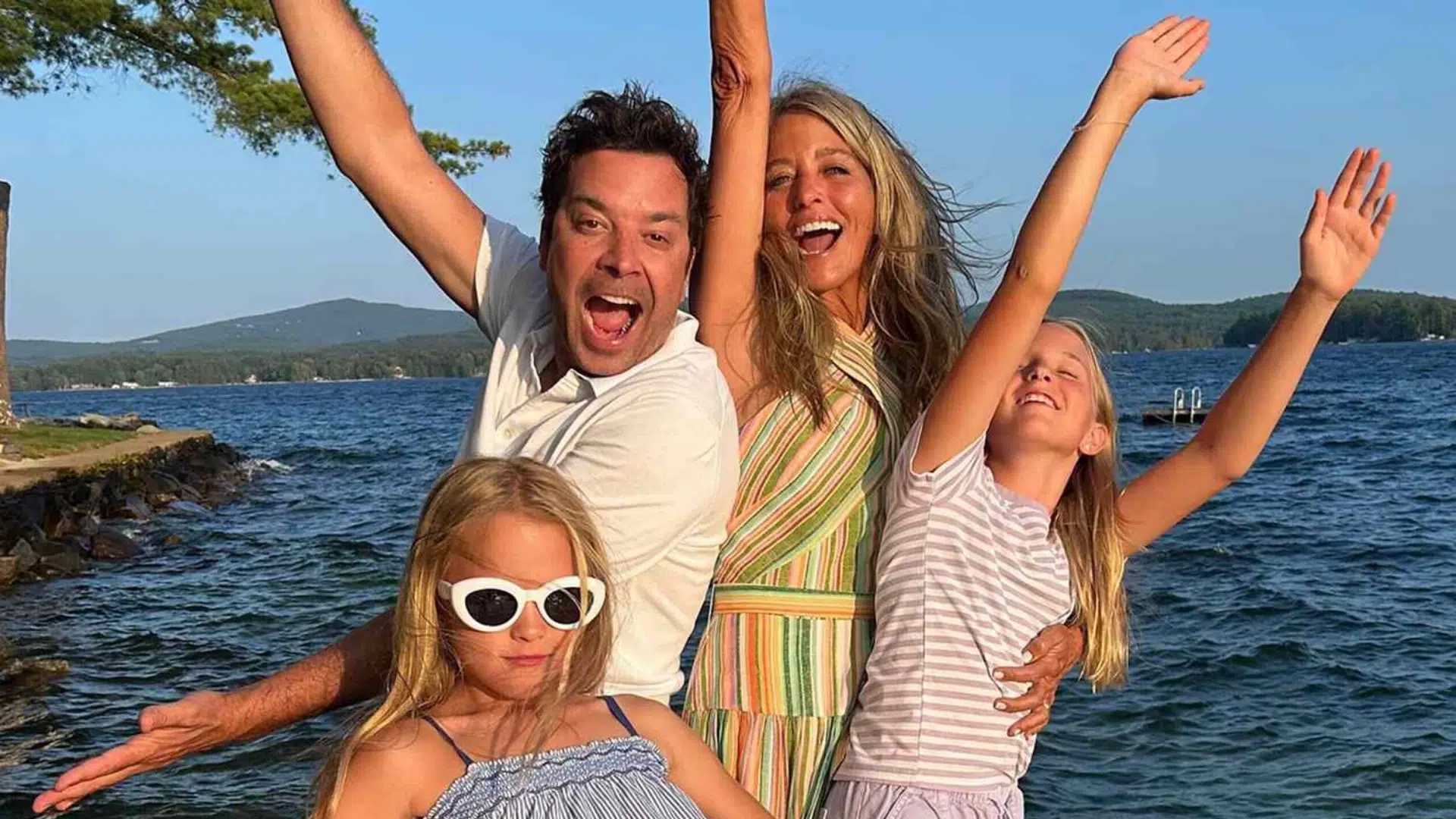 man and woman with two young girls posing together by a lake during a family vacation