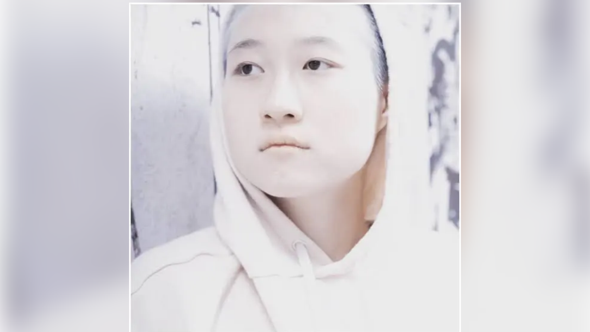 etta ng chok lam wearing a white hoodie and looking to the side in a softly lit portrait