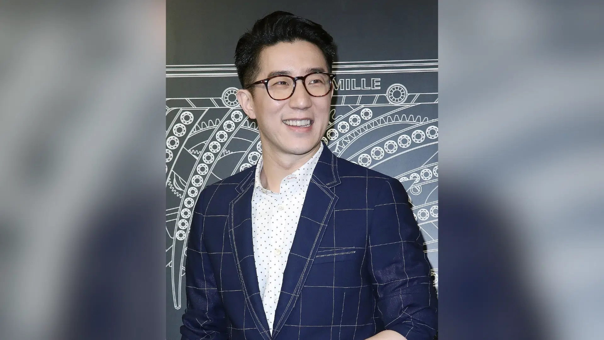 jaycee chan smiling in glasses and a navy checkered suit while posing at a formal event