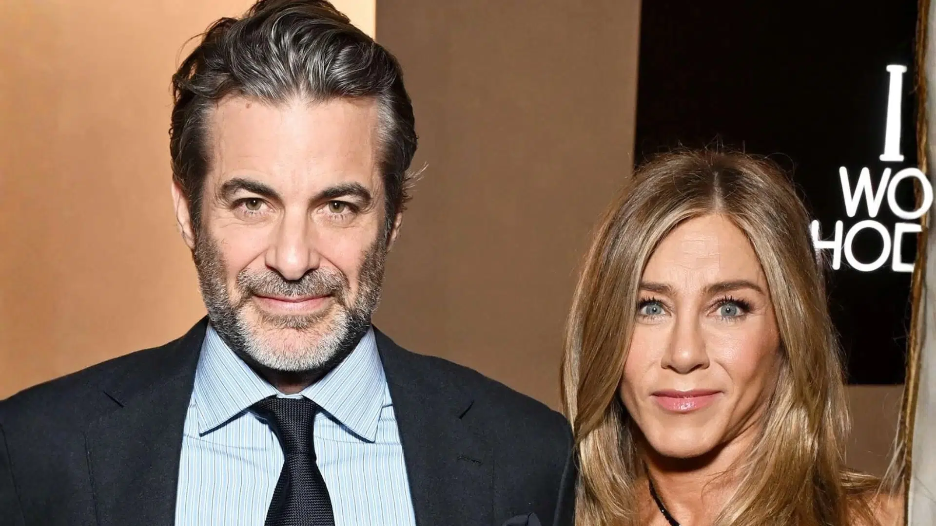 Jennifer Aniston and Jim Curtis posing together at an event with formal attire and a red carpet backdrop