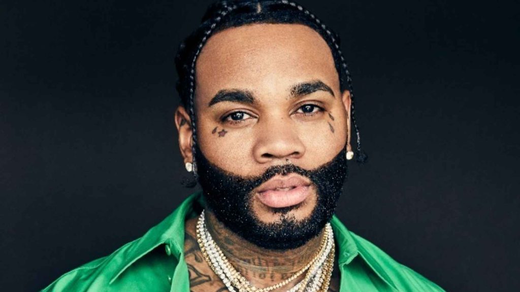 Kevin Gates wearing a bright green shirt and layered chains in a close-up studio portrait.