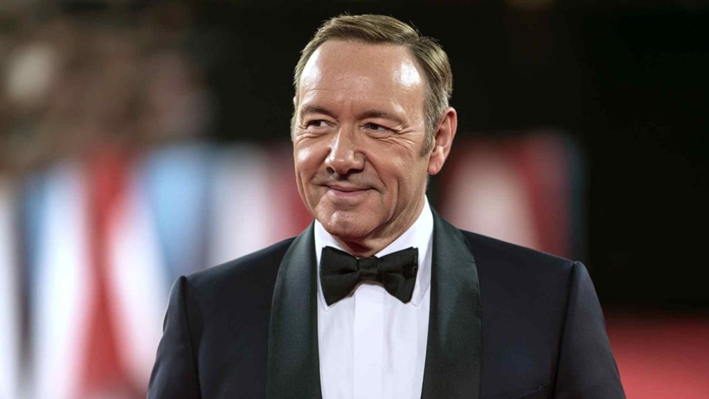 Kevin Spacey smiling in a black tuxedo with bow tie at a red carpet event