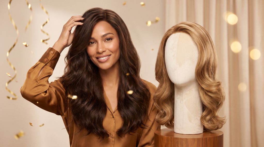 Woman with long brown hair smiling next to a blonde wig on a mannequin in a festive setting
