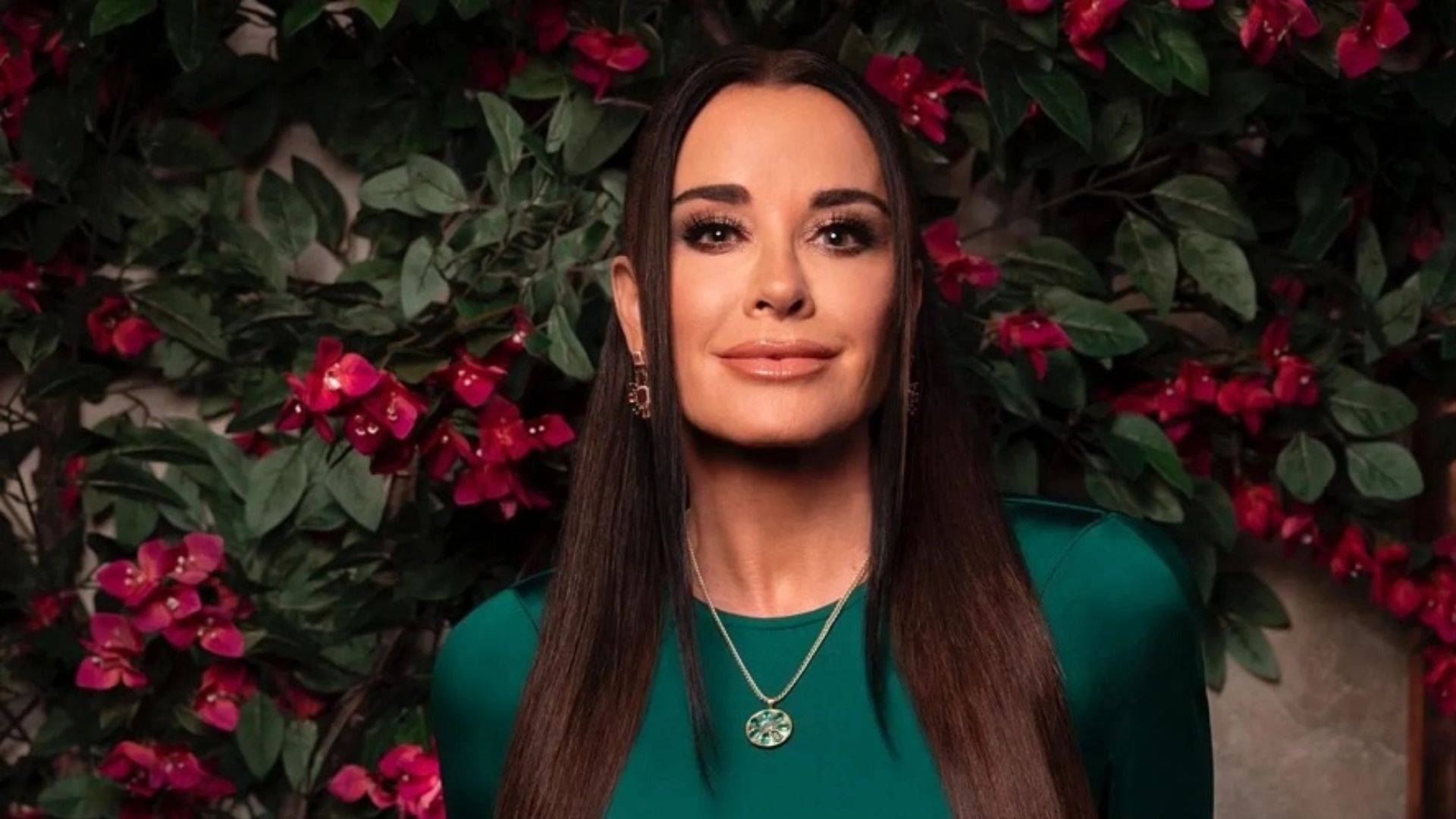 Kyle Richards posing in a green outfit with long dark hair against a floral background.