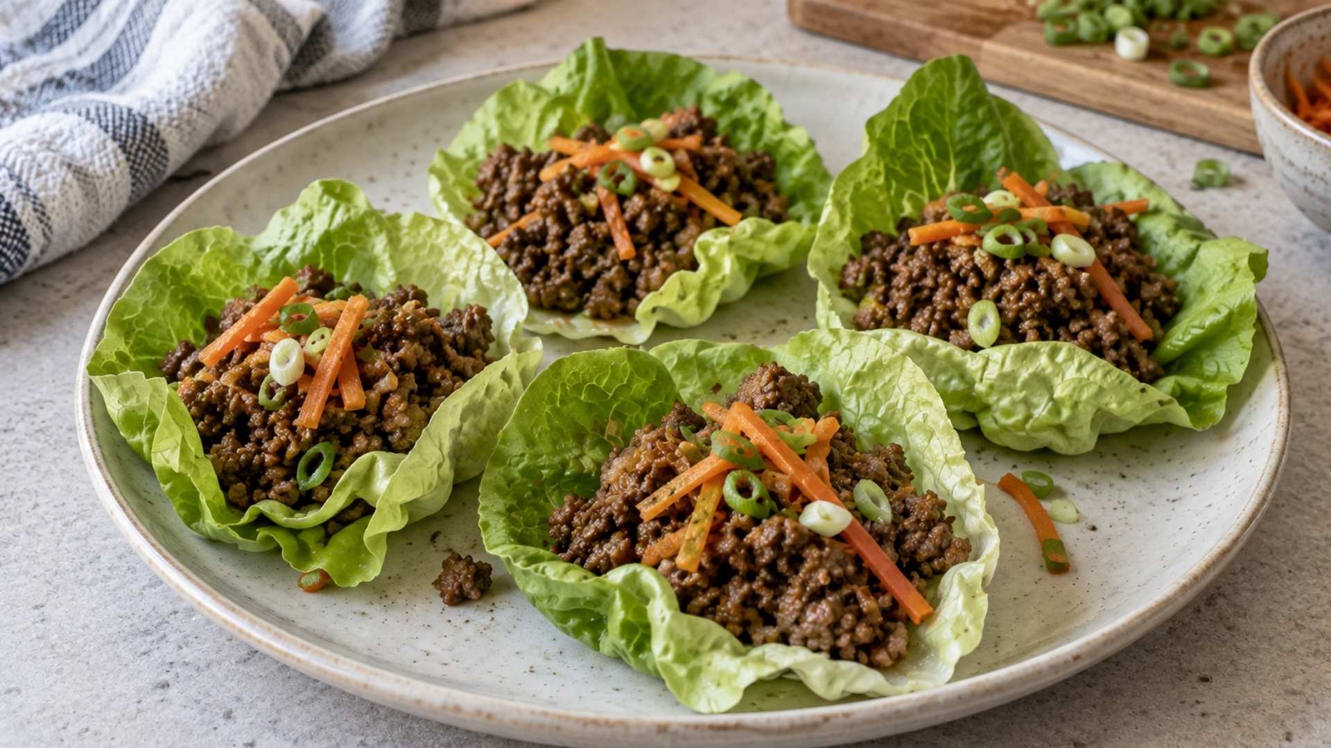 Beef lettuce wraps topped with shredded carrots and sliced green onions on a ceramic plate.