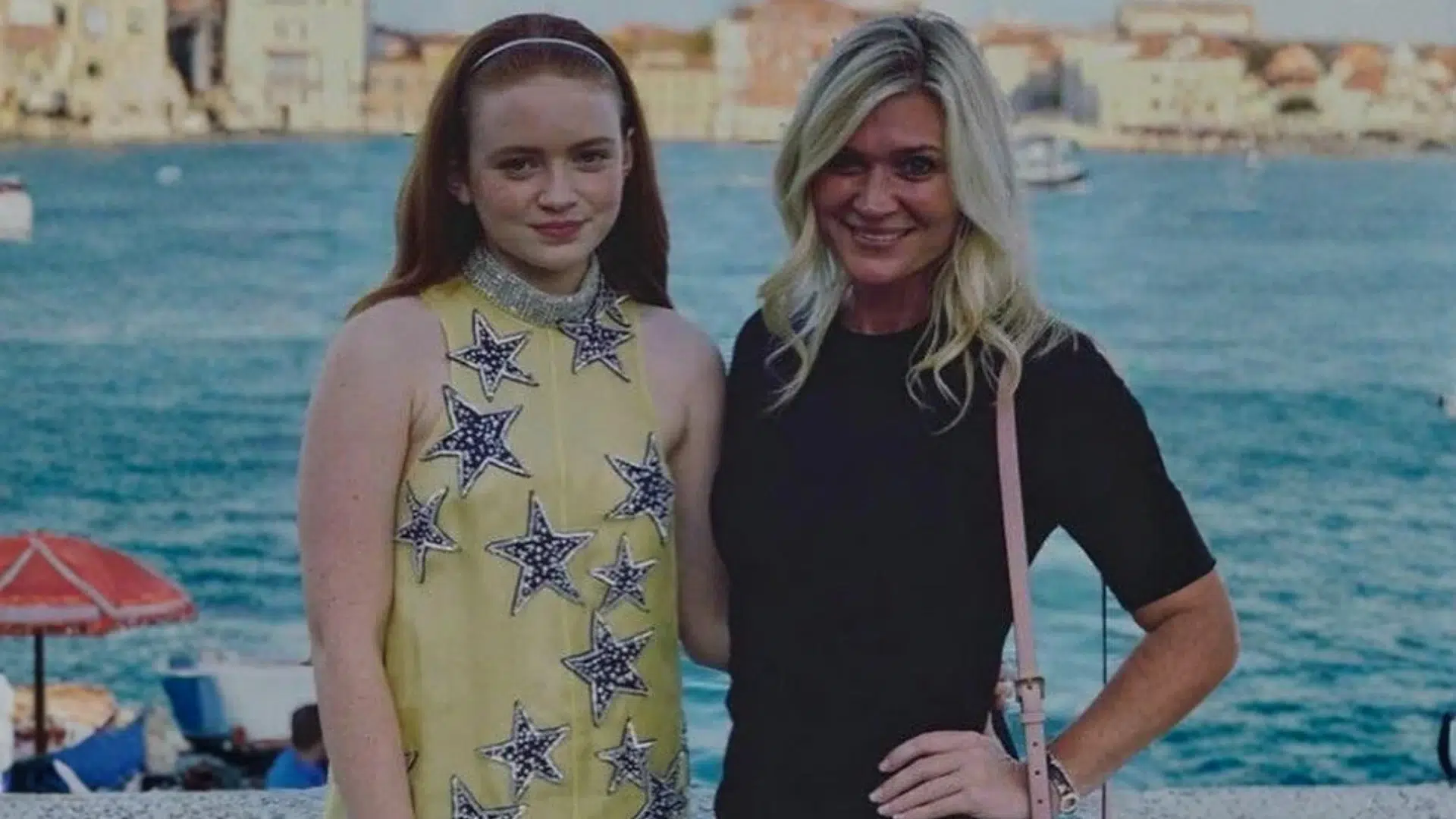 young woman in a yellow star-patterned dress posing with a blonde woman beside a sunny waterfront