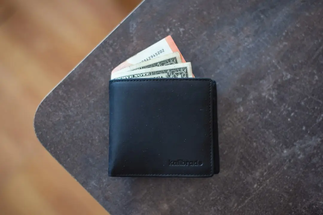 Black leather wallet with cash partially visible on a dark wooden table
