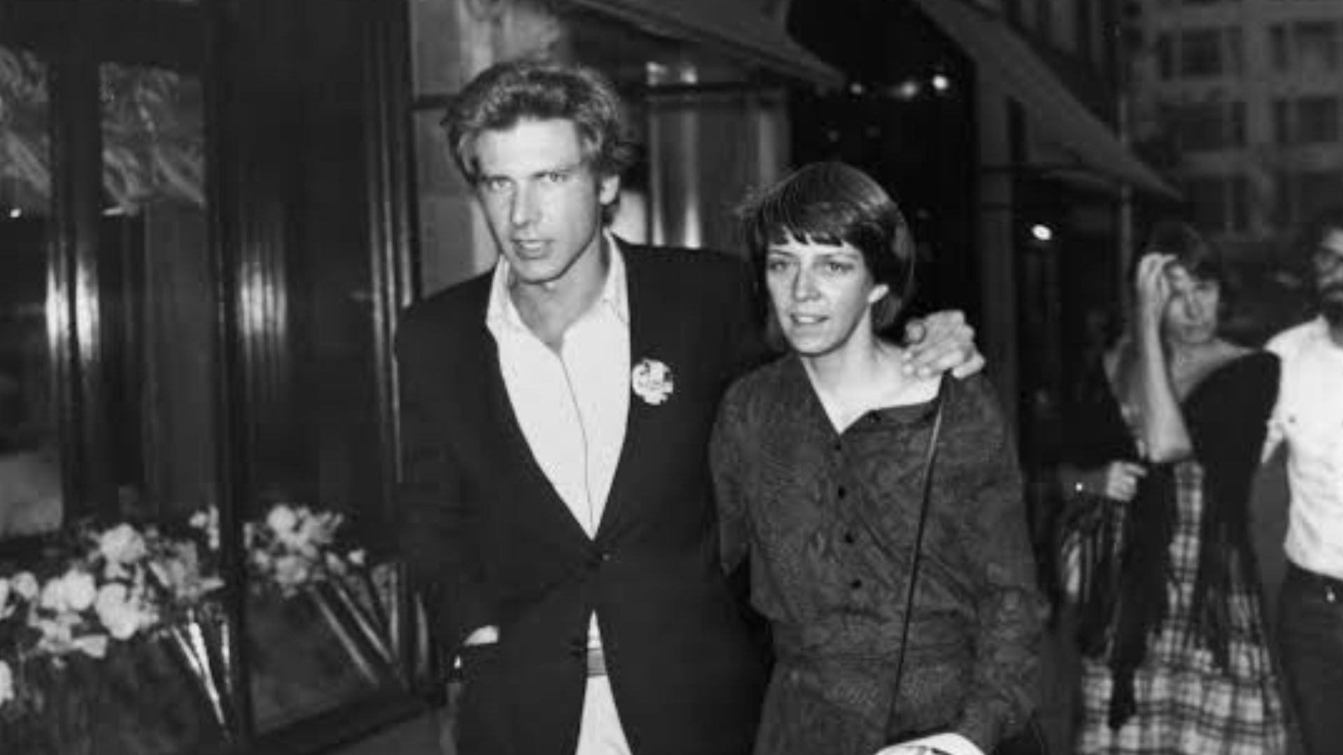 black and white image of harrison ford and mary marquardt in front of a shop
