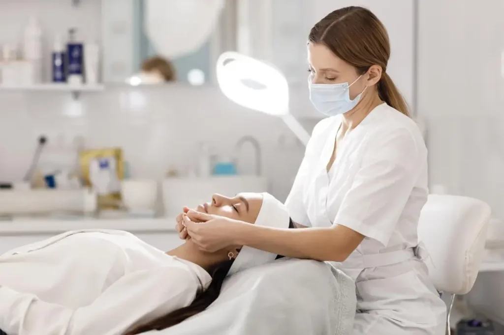 Esthetician performing facial treatment on woman in spa setting with bright lighting