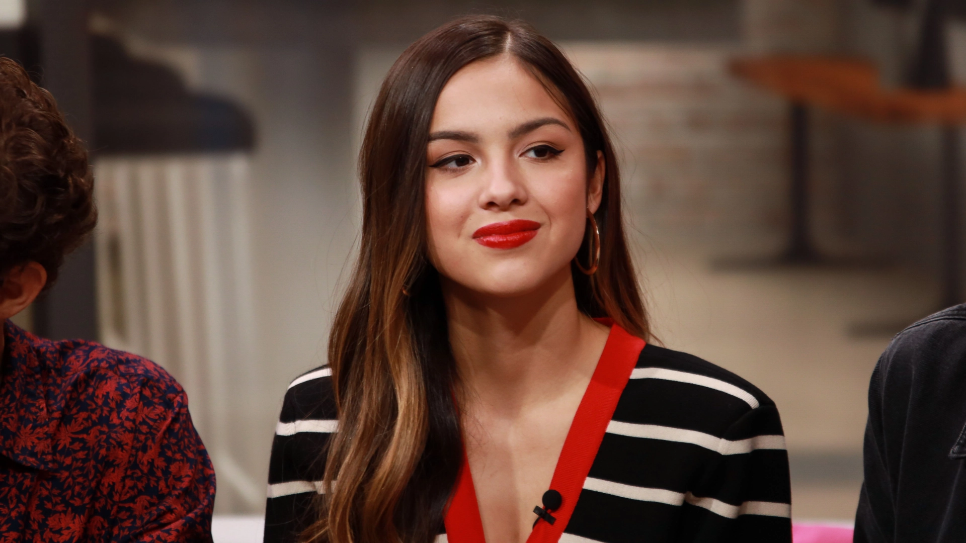 olivia rodrigo wearing a black and white outfit with red accents during an indoor interview or event.