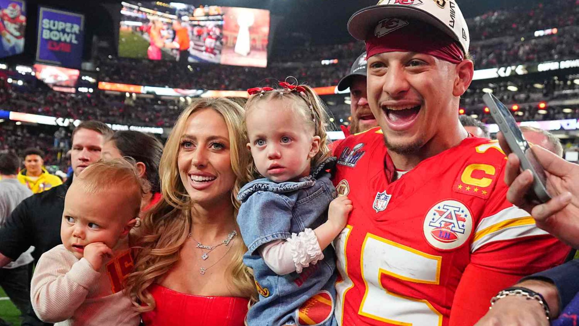 Patrick Mahomes posing with his wife Brittany and children on the football field after a game.