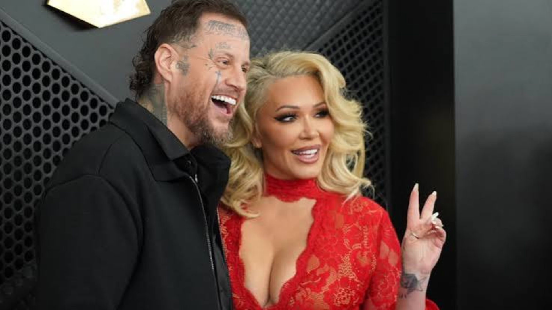 jelly roll and bunnie xo smiling together at an event, with him in black beside her wearing a red lace outfit indoors
