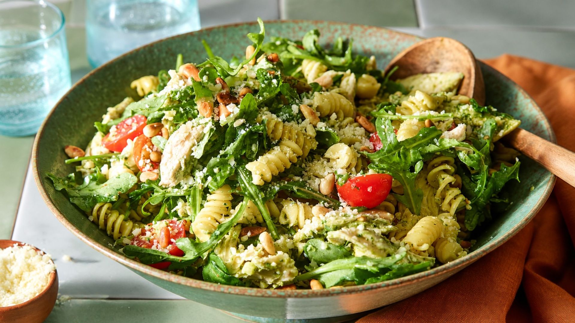 Pesto pasta salad with cherry tomatoes, spinach, peas and mozzarella in a light basil pesto coating.