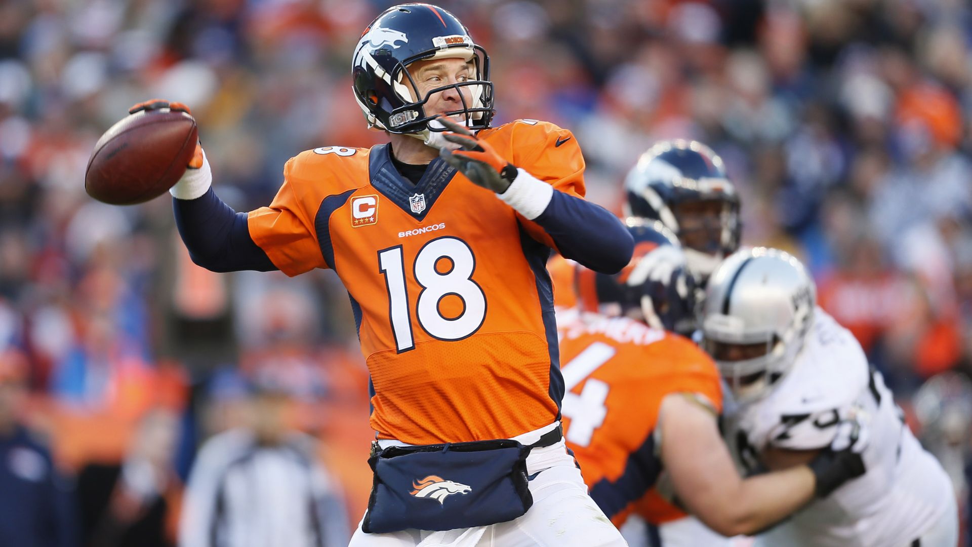 Peyton Manning in a Denver Broncos uniform throwing a football during an NFL game on the field.