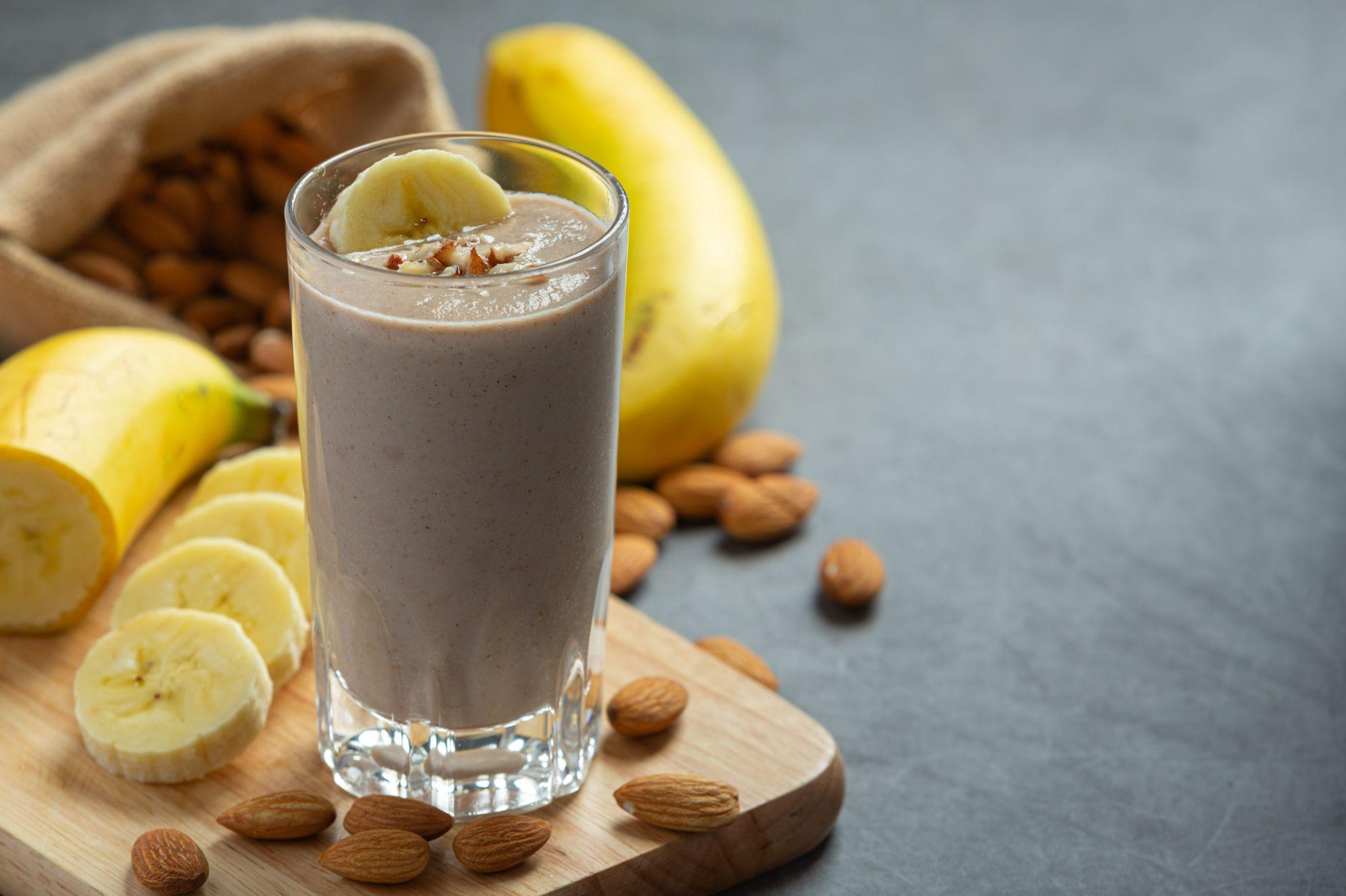 Banana almond smoothie in a glass on a wooden board with whole almonds and bananas