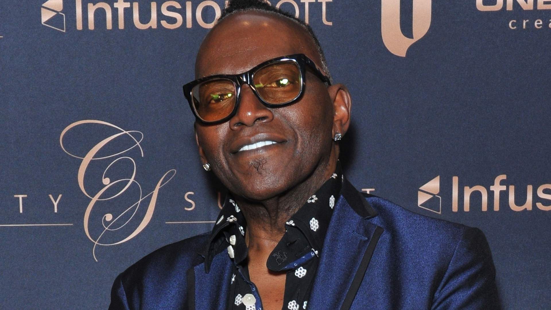 Randy Jackson wearing glasses and a blue suit at an entertainment event red carpet appearance.
