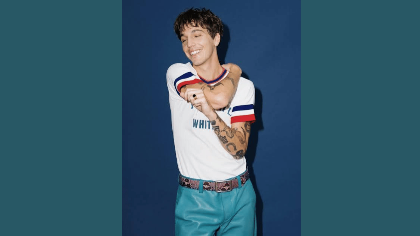 role model smiling in a white t shirt and blue trousers against a teal background