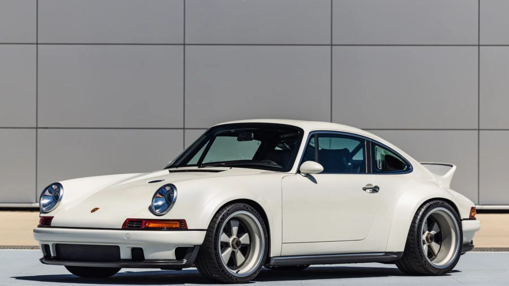 White classic Porsche 911 sports car parked in front of a modern gray building.