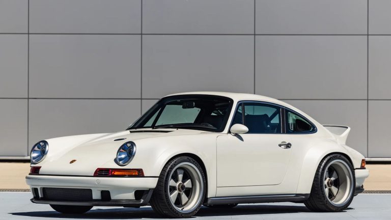 White classic Porsche 911 sports car parked in front of a modern gray building.