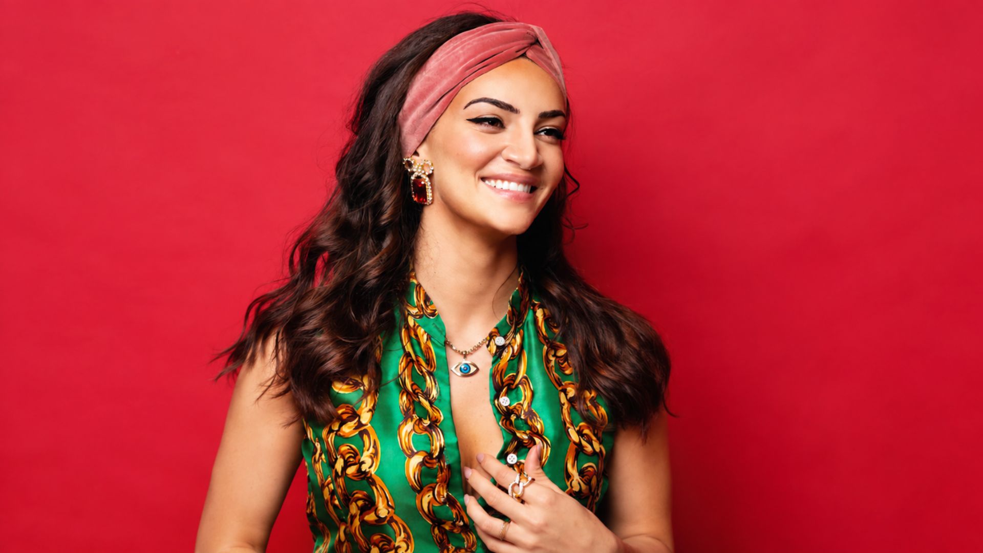 Sophie Brussaux, mother of Drake’s son Adonis, smiling in a studio portrait with a colorful outfit and red background.