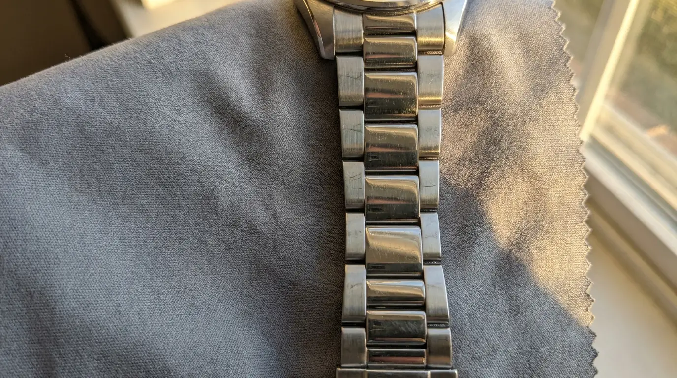 Silver metal watch strap resting on a gray cloth near a sunlit window