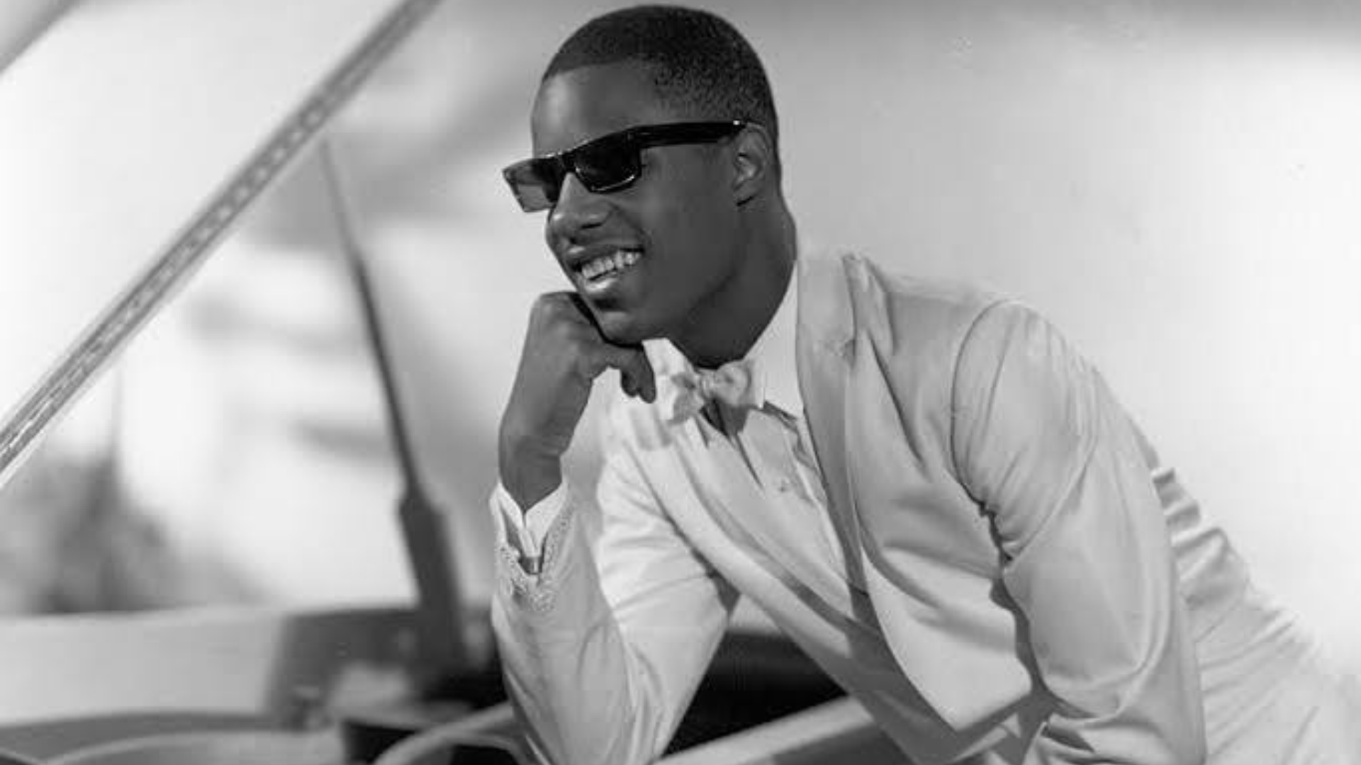 black and white portrait of stevie wonder wearing sunglasses and formal attire during a classic music era performance moment