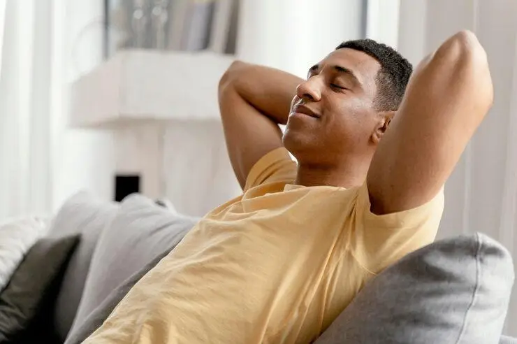 Person relaxing on a couch in a bright living room with closed eyes and a content expression