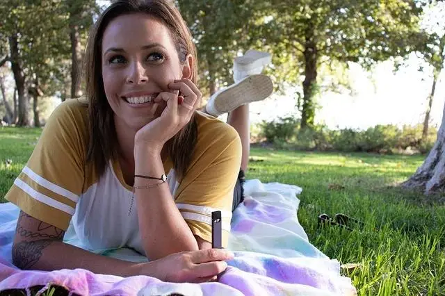 Woman in casual clothing lying on colorful blanket outdoors in sunny park
