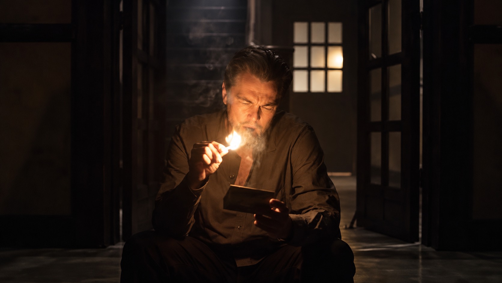 a still of Leonardo DiCaprio from the match of him holding a lit match and reading a card in a dark cinematic room with warm light and deep shadows