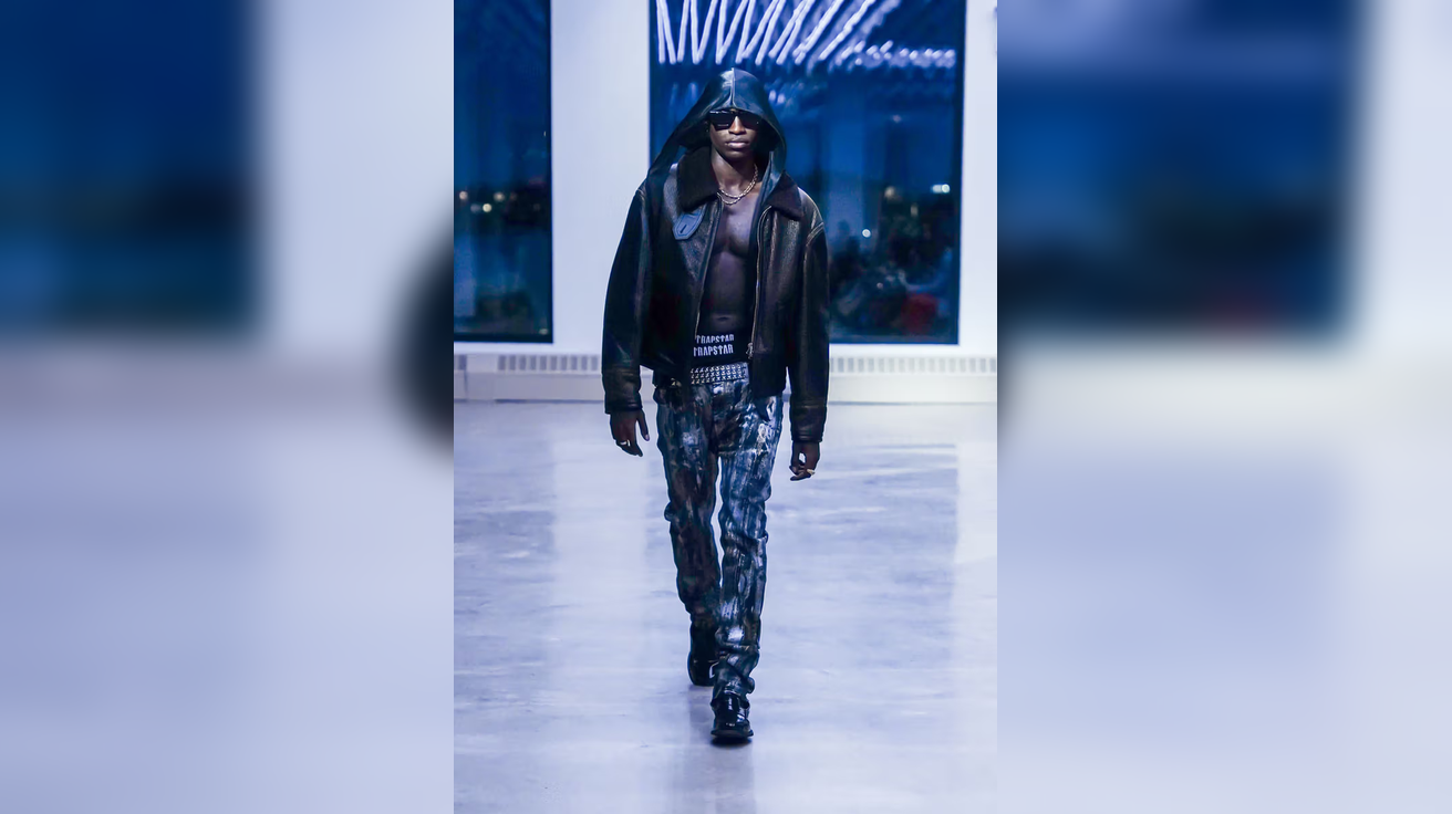 Model walking in dimly lit room wearing dark hooded jacket and patterned pants