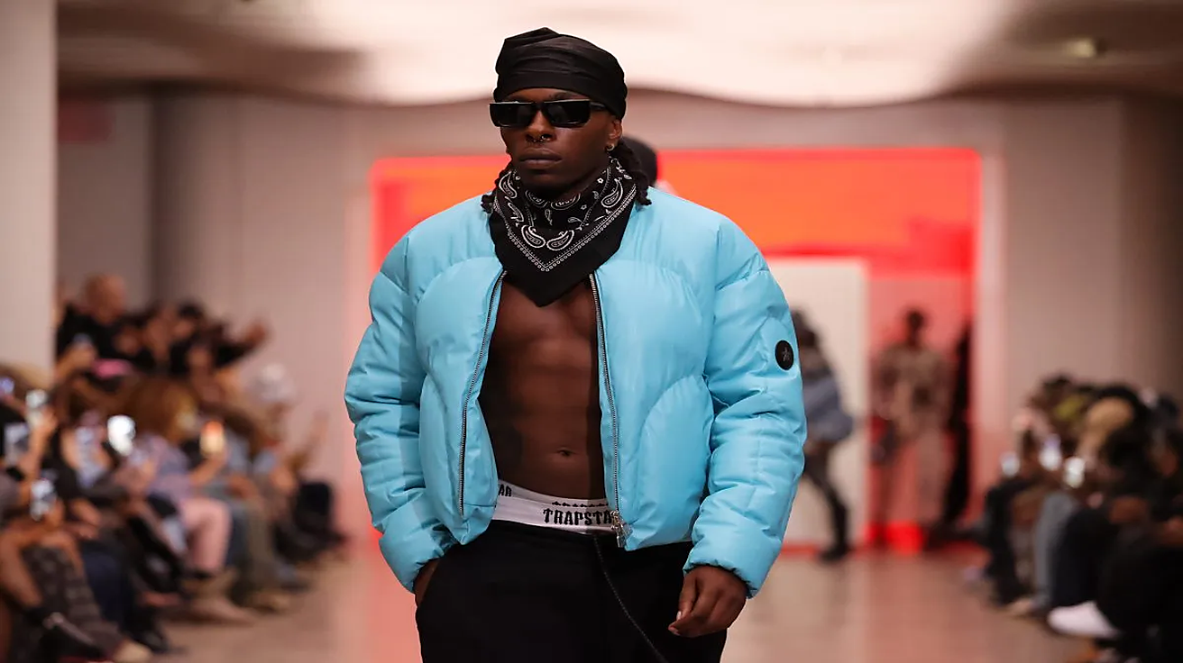 Model in blue puffer jacket and sunglasses walking runway in fashion show setting
