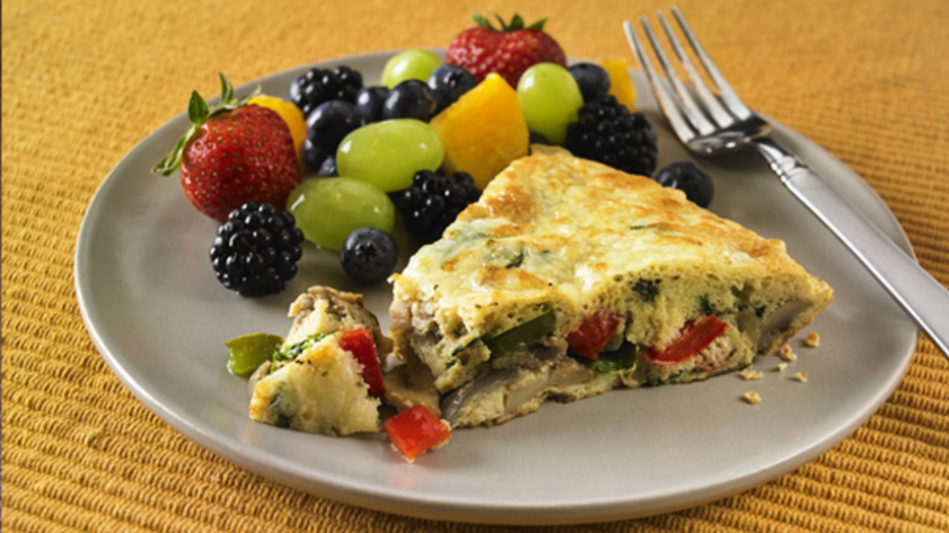 Vegetable frittata with spinach, peppers, tomato and onion served with a colorful side of fresh fruit.