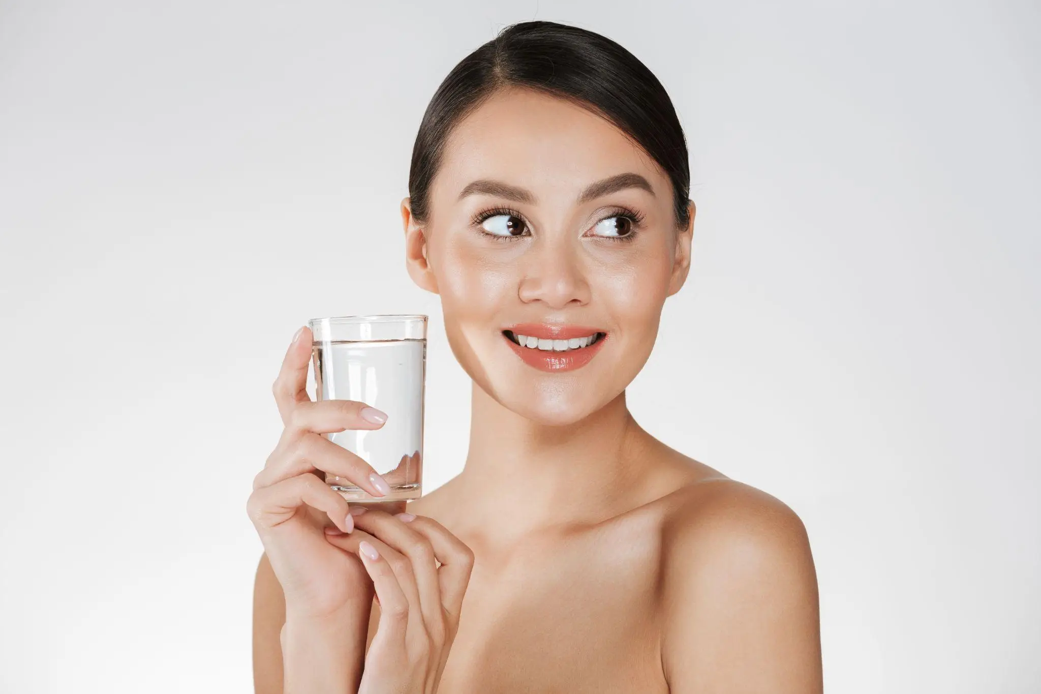 Woman holding a glass of water smiling against a plain background