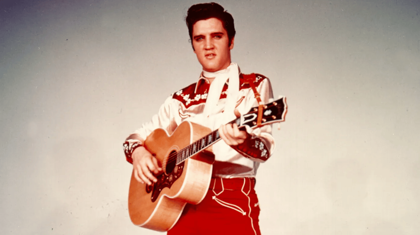 young elvis presley wearing a western outfit while holding his guitar