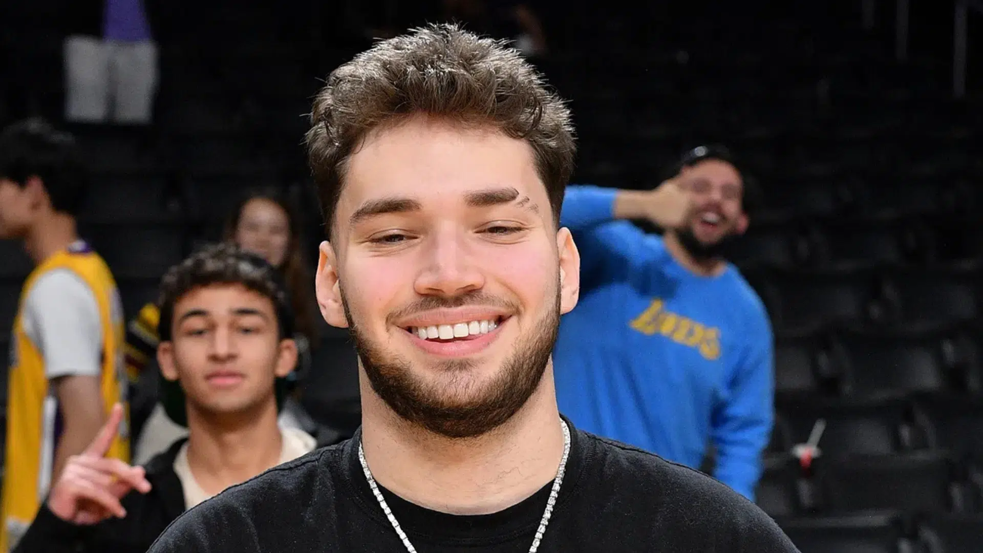 close-up of a smiling young male streamer at a basketball arena, with several people blurred in the background