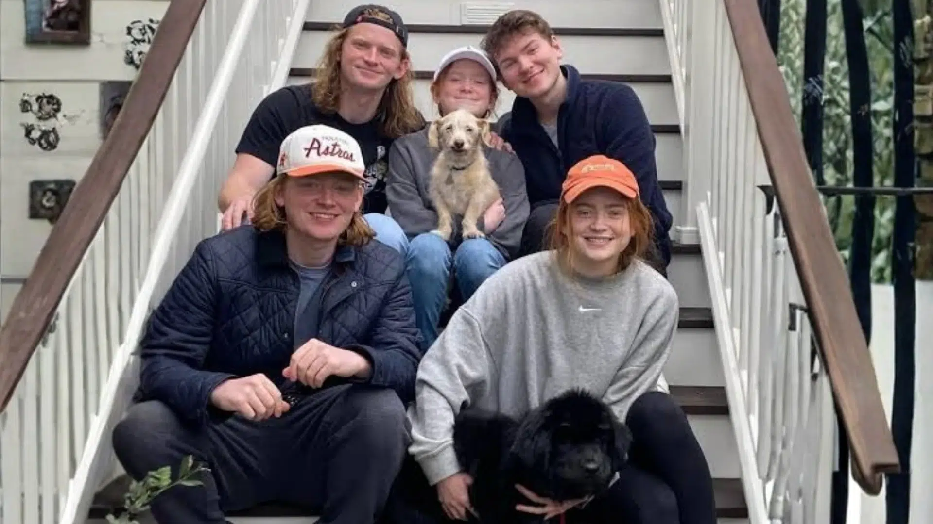 five young people sitting on outdoor steps, with one holding a small tan dog and another holding a black dog