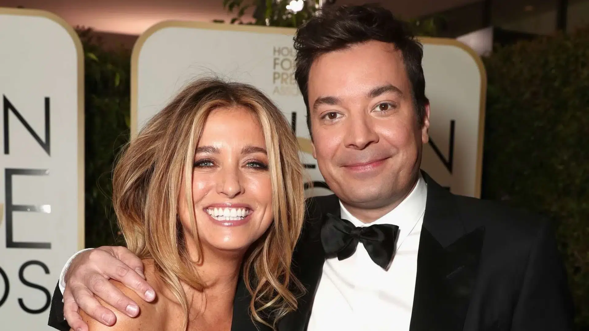 Jimmy Fallon and his wife smiling together at a formal event with a decorated backdrop behind them