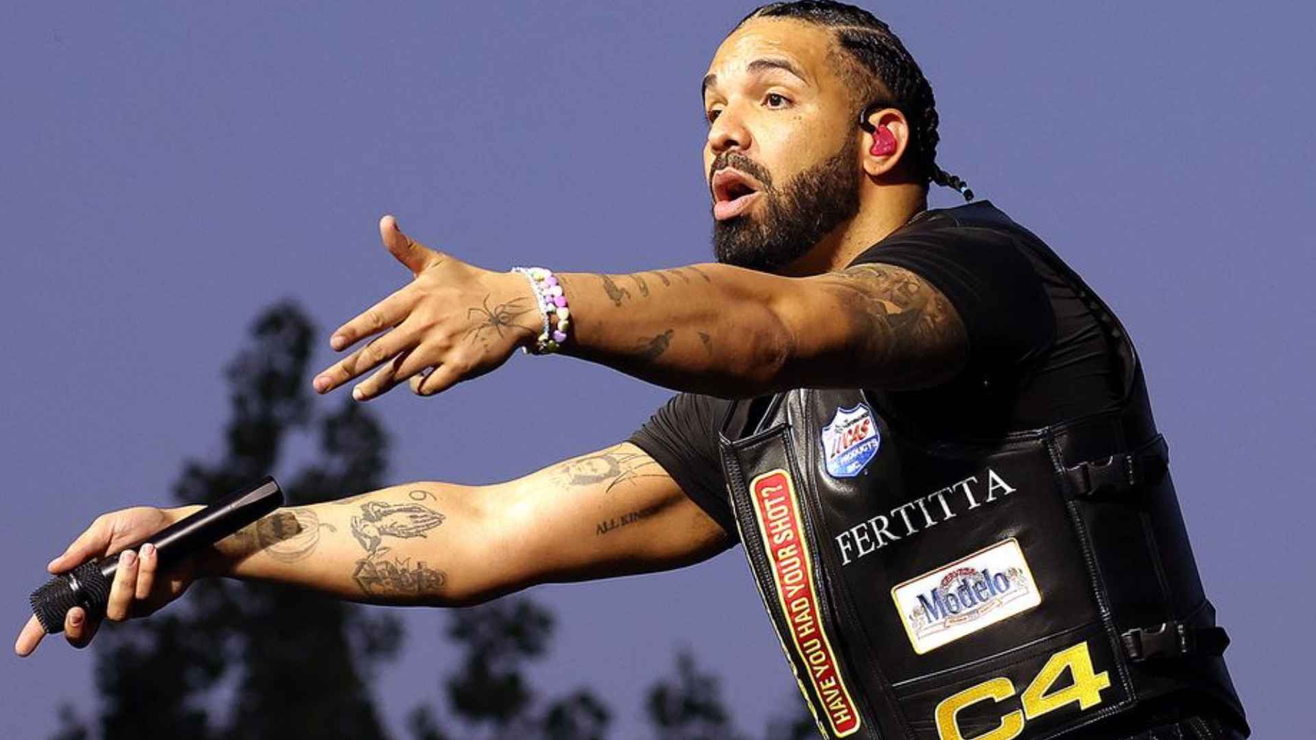Drake performing on stage while wearing a black outfit and holding a microphone during a live concert.