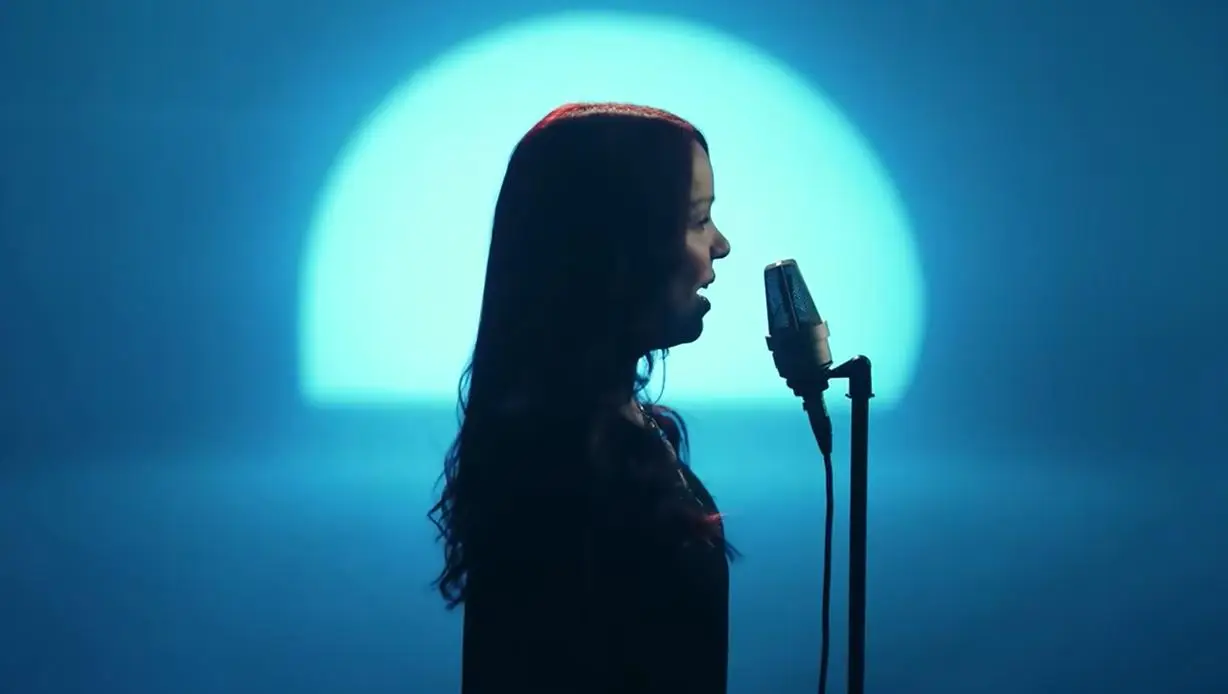 Singer performing into a microphone against a blue-lit circular background