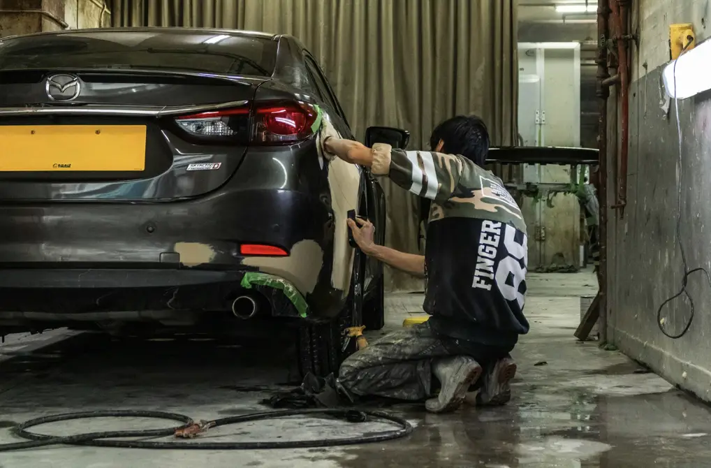 Mechanic repairing dent on black car in an indoor workshop setting