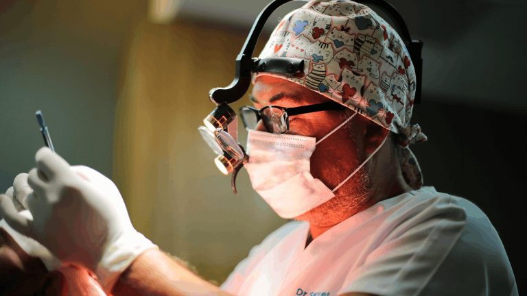 Surgeon wearing patterned cap and mask performing surgery with precision in dimly lit room