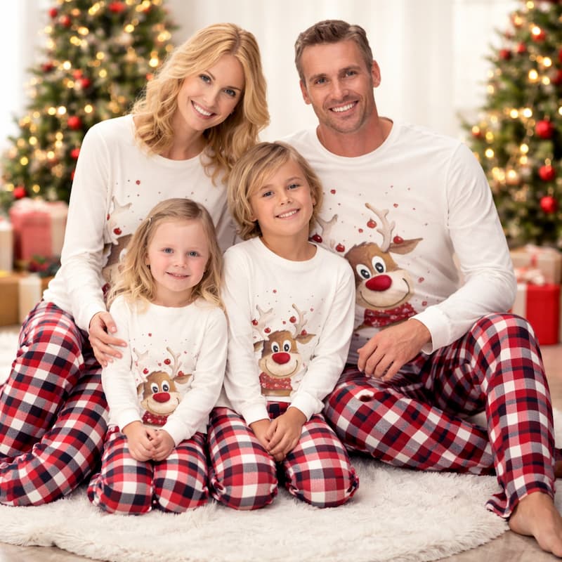 Family in matching holiday pajamas sitting together by Christmas tree indoors